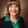 Woman in green shirt with blazer smiling in front of a brown background