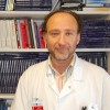 Man standing in front of book shelves he is wearing a white coat 