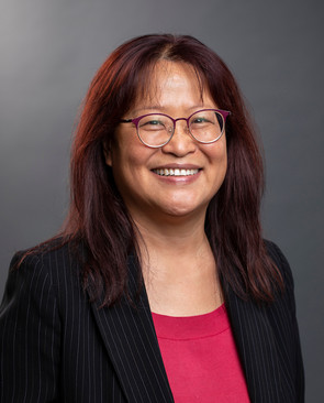 Woman smiling. She has brown hair and wears glasses. She is wearing a red shirt and black sport coat